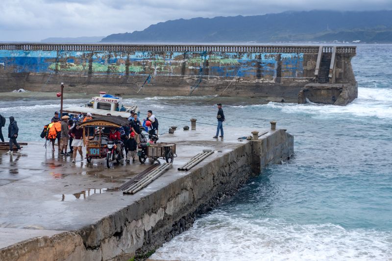 The port itself, with the small ferry still unloading. Tricycles and motorcycles are the main mode of transportation here, and gas prices are fixed and don't follow the usual fare. Batan is seen in the distance. The seawall behind it has since been significantly damaged half a year later, in September 2025.