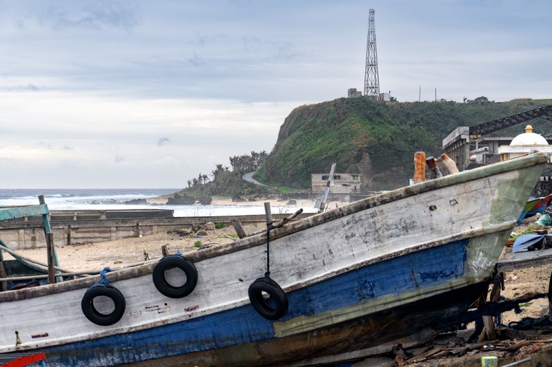 A beached ferry. An active construction site can be seen on the right, as well as a communications tower in the background. Taken near Sabtang Port.